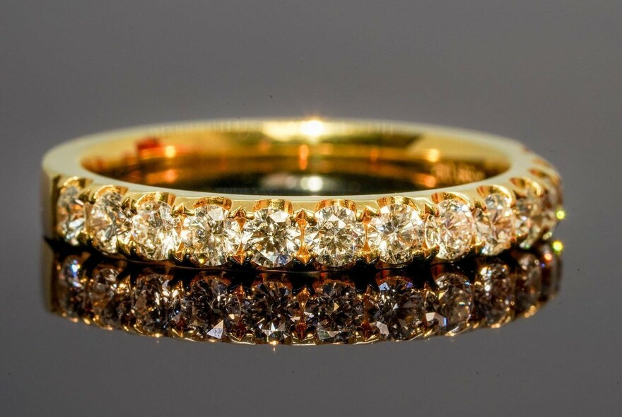 Gold ring with inset row of diamonds, reflected in mirrored glass.