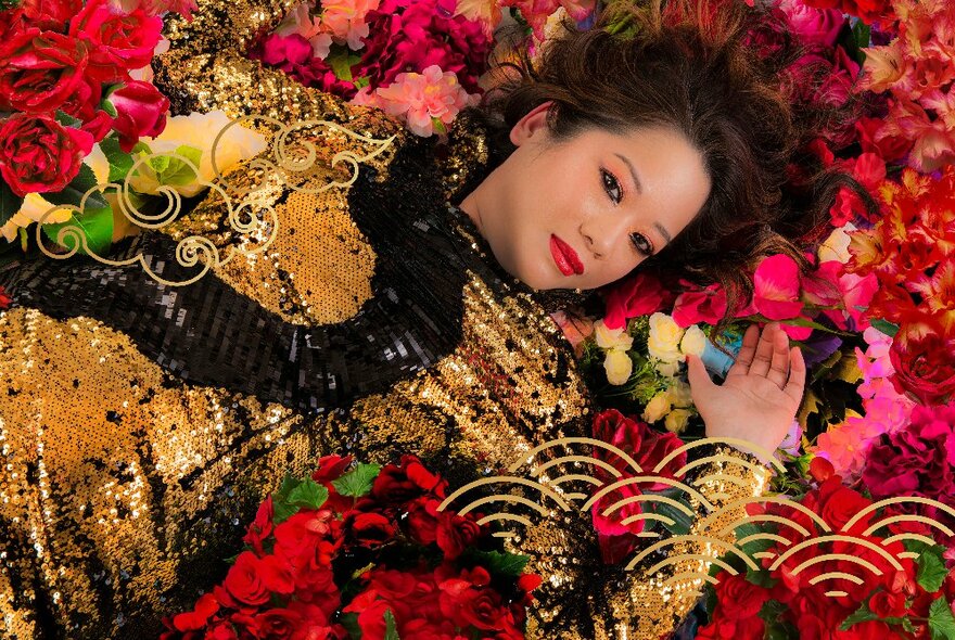 Woman lying in a bed of rose petals, wearing a gold dress with cloud details.