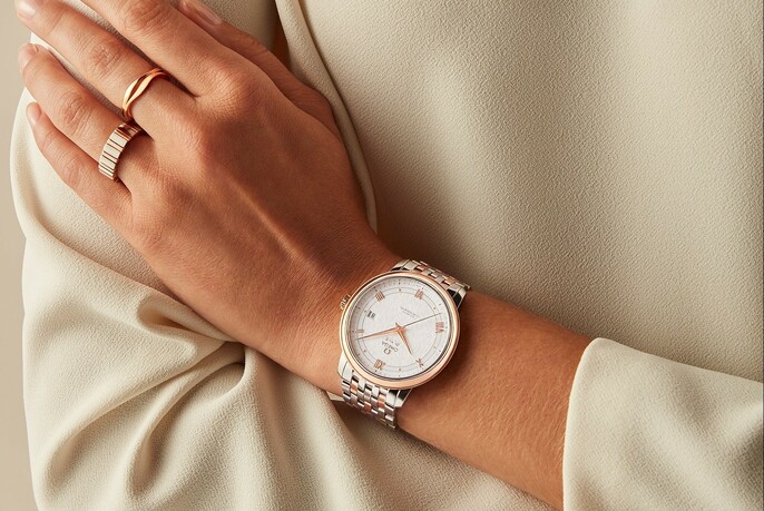 Watch on a person's wrist crossed against other arm, in cream clothing.