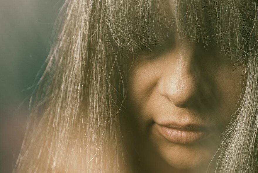 A woman's face, partially obscured by her straight hair and fringe, looking down.