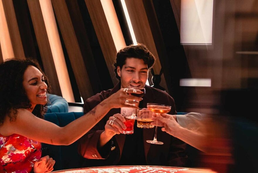 People smiling and raising their glasses in a toast, seated around a table in a club.