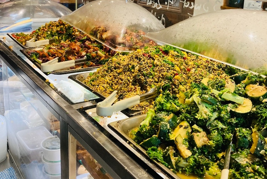 Large stainless steel containers of mixed vegetable salads on display in a cafe.