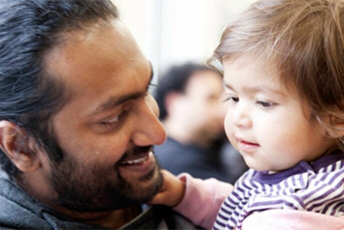 Man smiling and looking intently at the face of a young toddler he is holding in his arms.