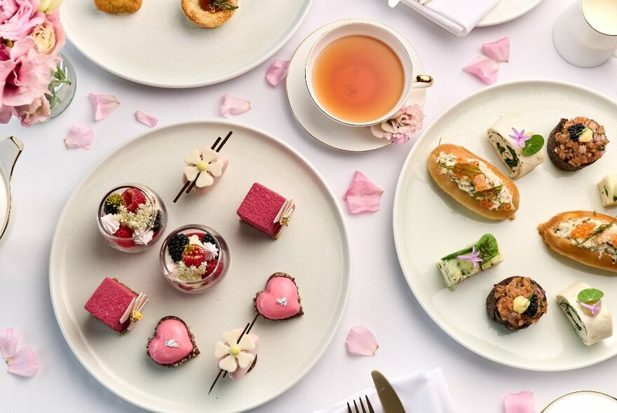 Looking down at a table with plates of dainty little canapés and petit fours, all in pink tones with tea on the side. 