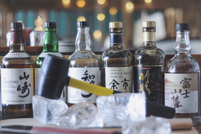 Row of sake bottles with chunks of ice and small mallet in front.