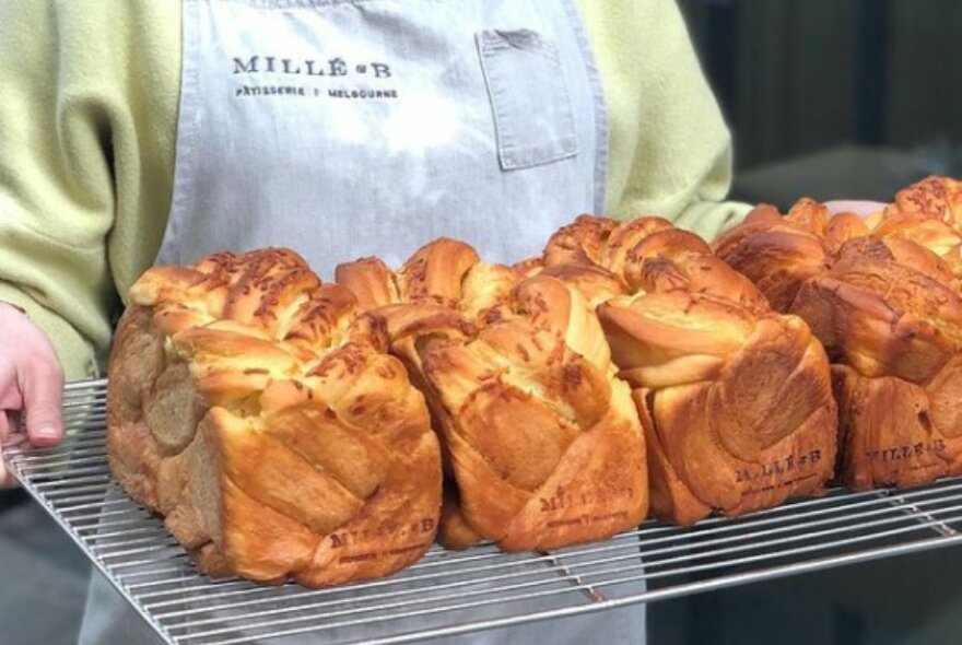 Someone in an apron carrying a tray of twisted shokupan loaves.