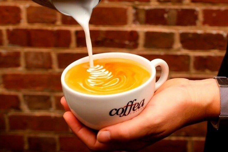 Hand holding a coffee cup, pouring milk into a latte.