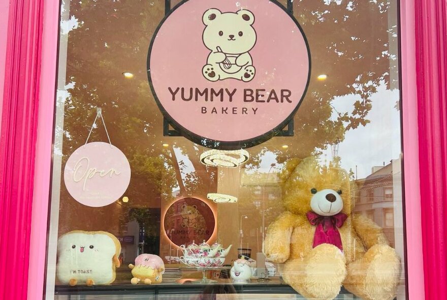 A shopfront window with fluffy bears sitting on a shelf and the pink Yummy Bear Bakery sign in the centre.