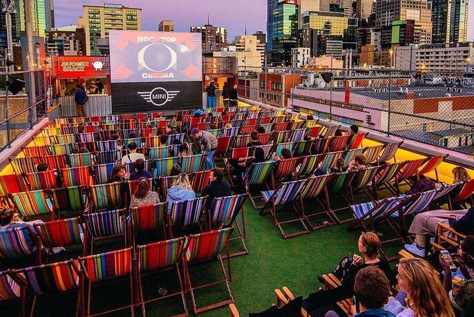 Multi-coloured deck chairs all facing the Rooftop Cinema screen with city skyline visible in the distance.