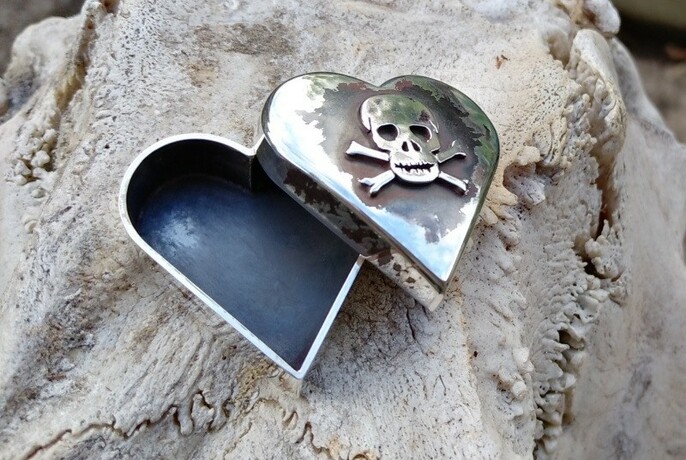 Heart-shaped metal box with skull and cross bones on it.