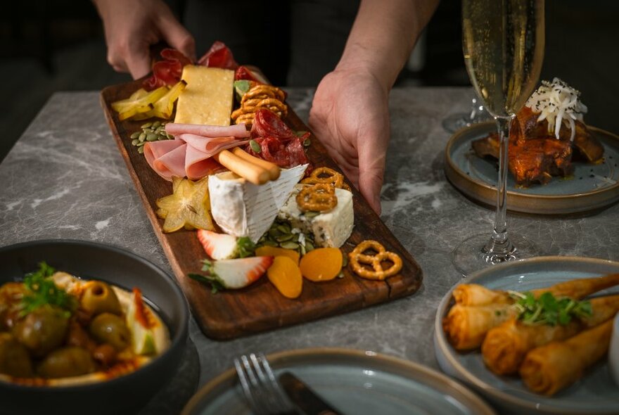 A waiter placing an antipasto platter of cheese, cured meats and dried fruits onto a dining table.