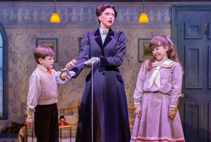 Actors dressed as Mary Poppins and the two children in a Victorian stage set.