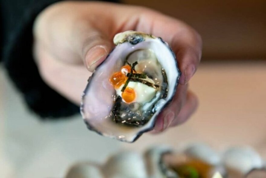 Person holding an oyster with salmon roe garnish.