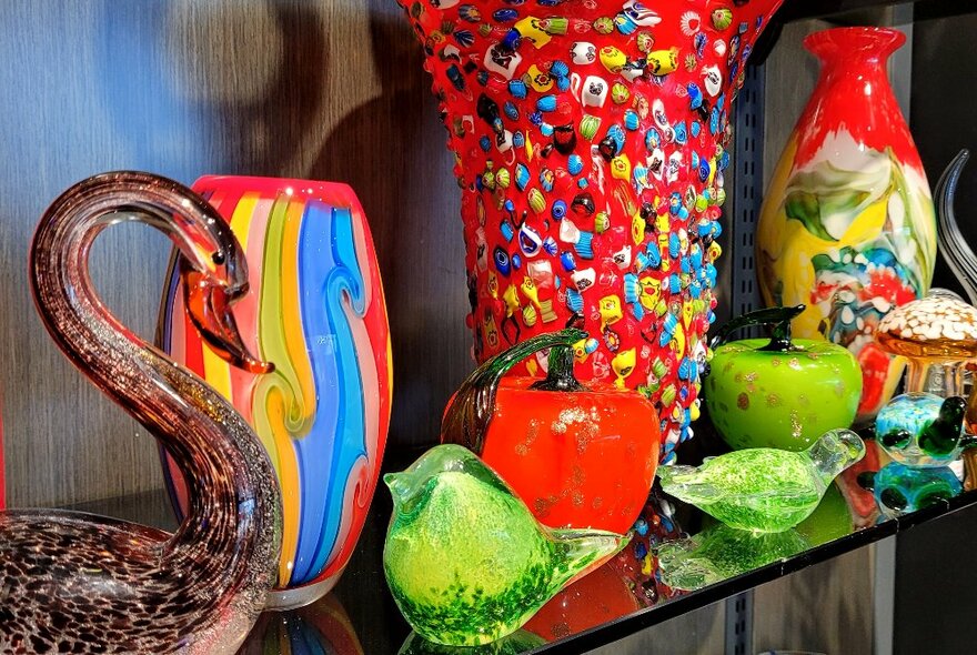A selection of colourful glass vases and statues displayed on a glass shelf.
