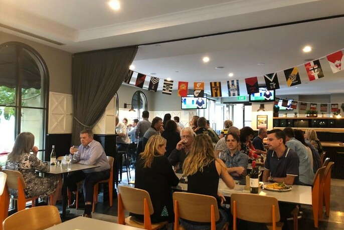 Restaurant interior with diners at tables, footy flags hanging from the ceiling.