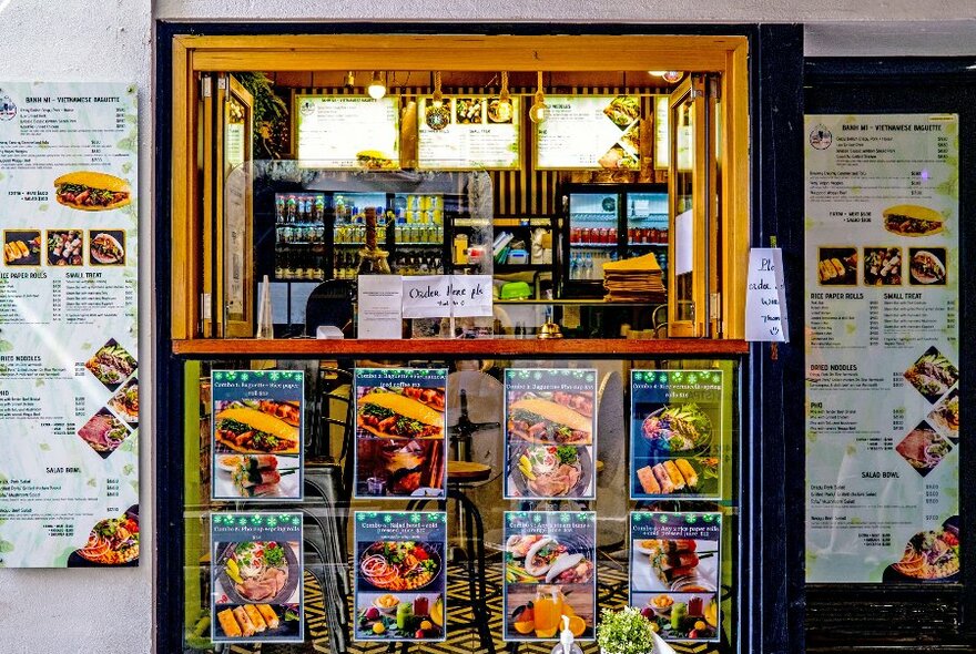 The exterior of a small Vietnamese pork roll shop with picture menus surrounding the window.