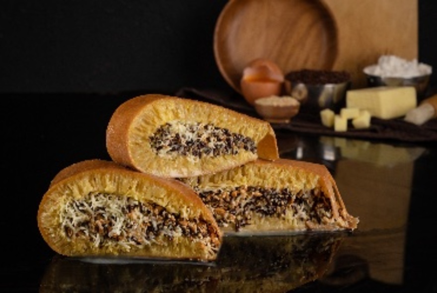 Three rolled Indonesian martabak, a dense pancake with different fillings, piled on top of each other on a dark table.