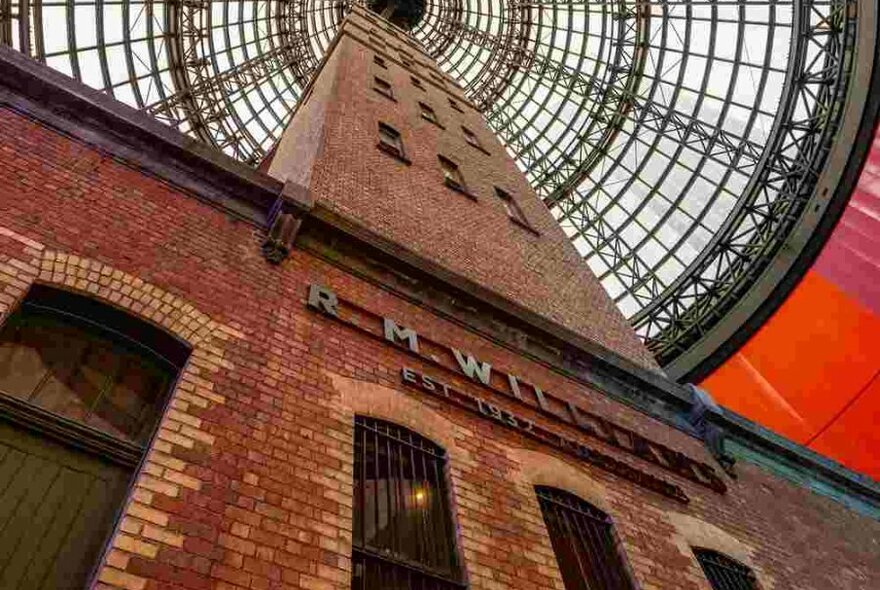 A tall brick structure inside a shopping centre with a glass dome surrounding it.