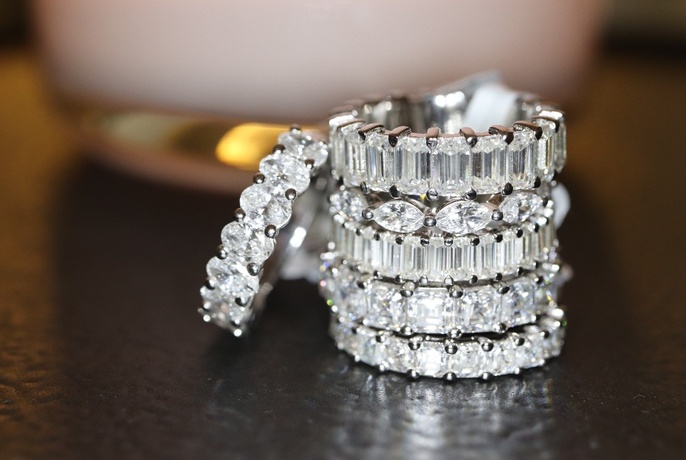 Pile of sparkling diamond rings with one ring resting up against the pile on left.