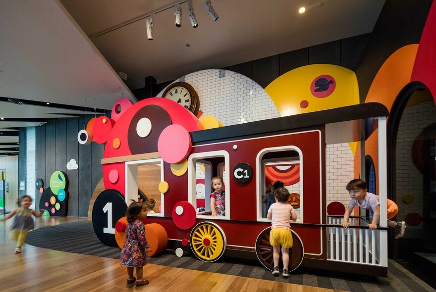Young children playing indoors on large stylised toy train.