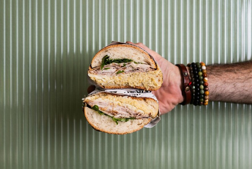 A hand holding a ham panini in front of a cream-coloured fluted wall.