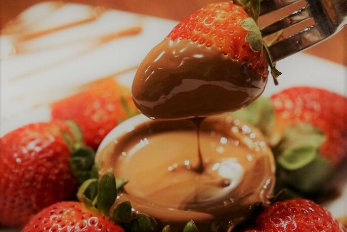 A fork dipping strawberries into a pot of chocolate.