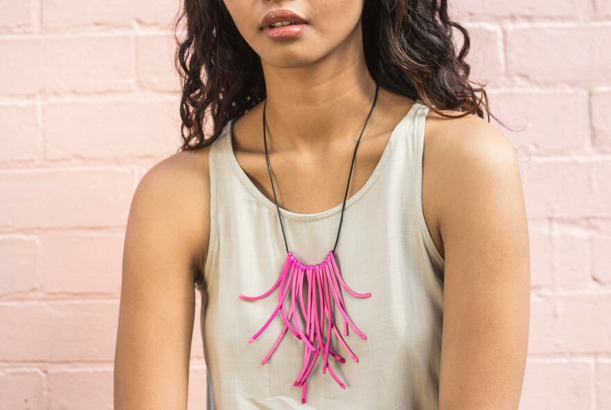 Woman wearing a white singlet with a bright pink necklace.