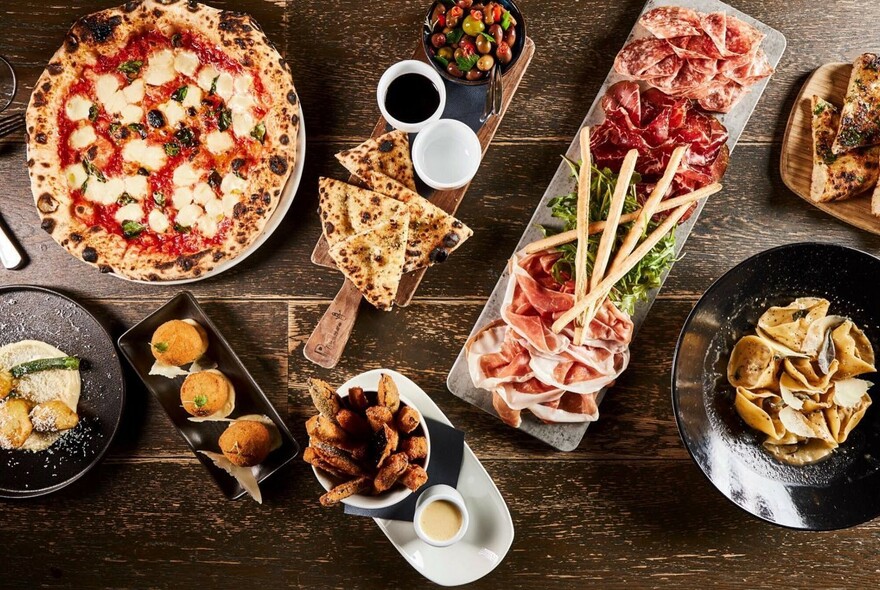 A grazing antipasto platter, pizza and other savoury food arranged on table.