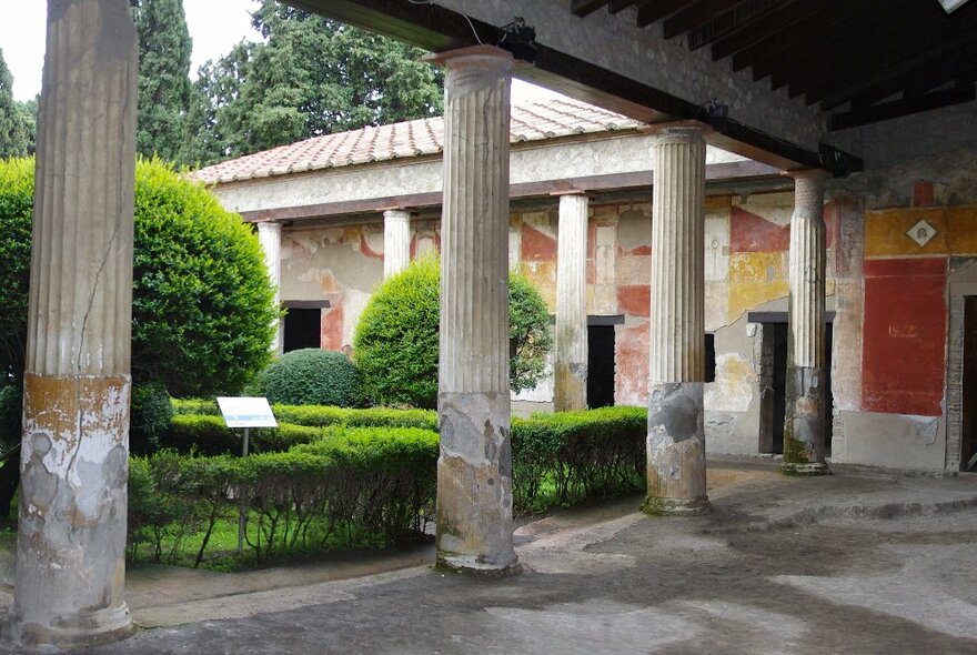 An example of ancient Roman architecture, highlighting the pillars of a covered portico and surrounding manicured garden.