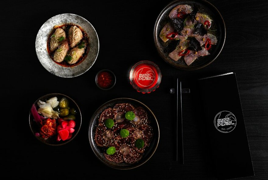 Overhead view of dishes of food and drinks on a dark table.