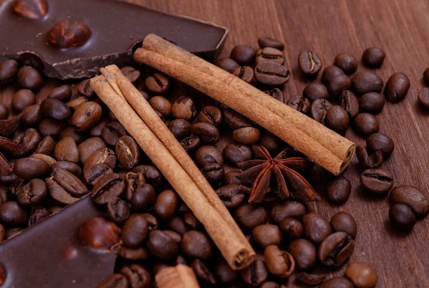 Pieces of dark chocolate, cinnamon sticks and star anise on a wooden background.