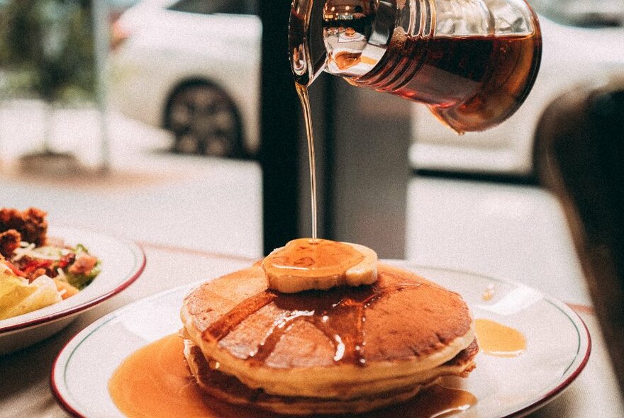 Maple syrup being poured onto a stack of pancakes.