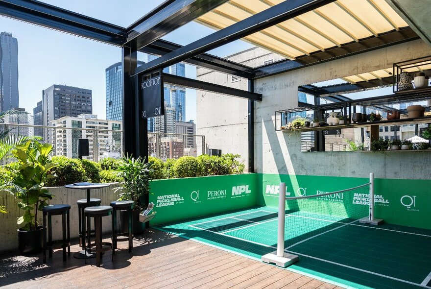 A pickleball court at the rooftop bar at QT Hotel in Melbourne, with the city skyline in the distance.