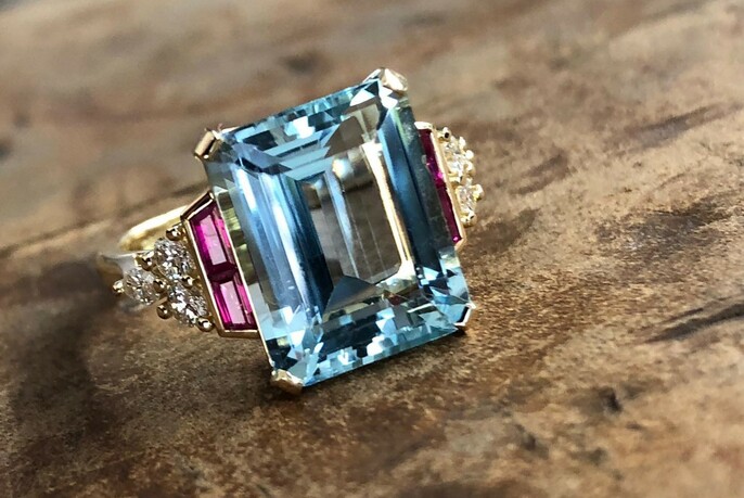 Gold art-deco-style ring with large central square-cut aquamarine set off by diamonds and rubies.