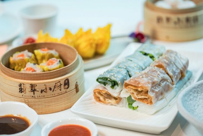 Asian dishes on a table, including steamer with dumplings, condiments and wraps.