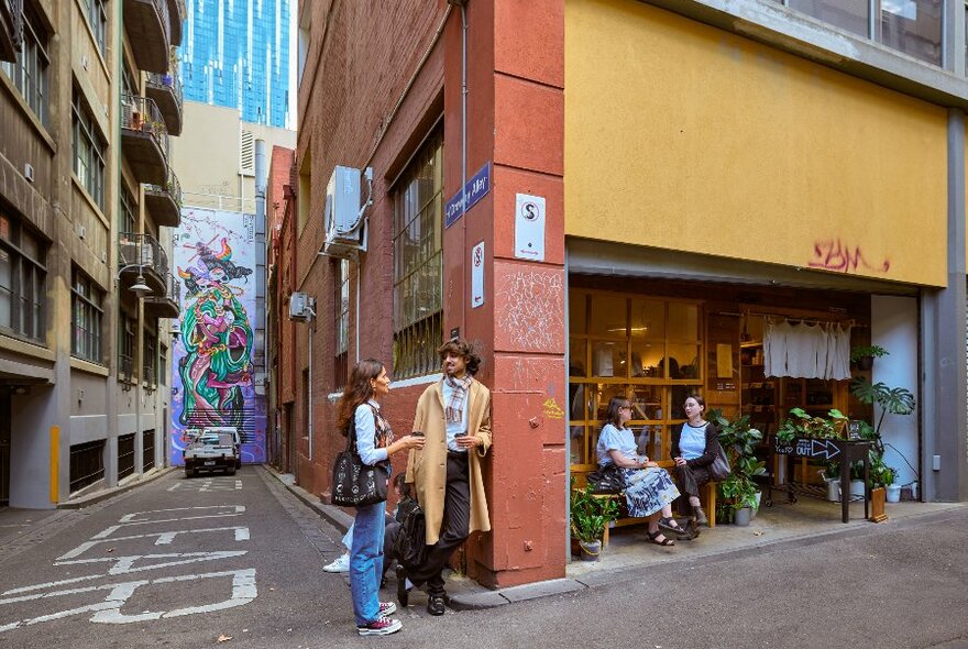 Four friends are outside a laneway cafe there is street art on the wall