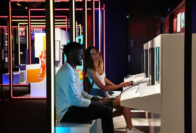 Man and a woman playing game in low lit exhibit with neon lights.