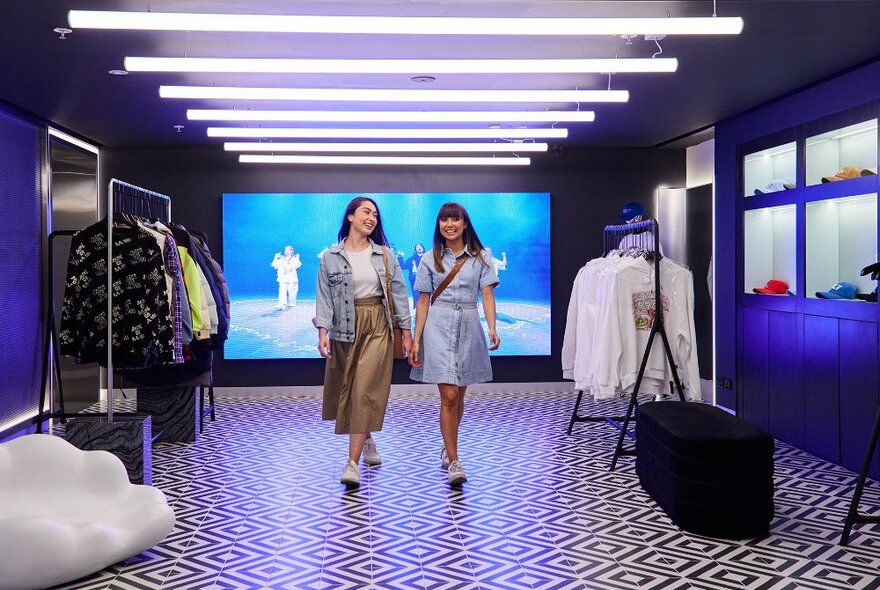 Two women working through a retail store with patterned floors and a blue screen behind them.