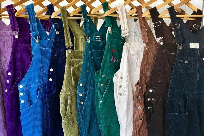 Rows of blue and green dungarees hanging on hangers.