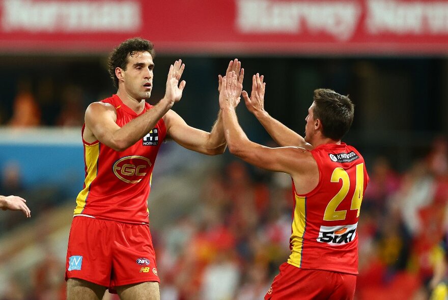 Gold Coast SUNS AFL football team members high-fiving during a match.