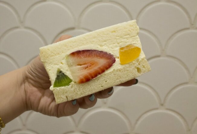 Hand holding fruity cream sando on it's side, showing inside filled with cream and fruit.