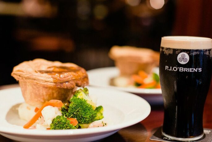 Pie and vegetables on a plate, with a pint of dark stout next to it.
