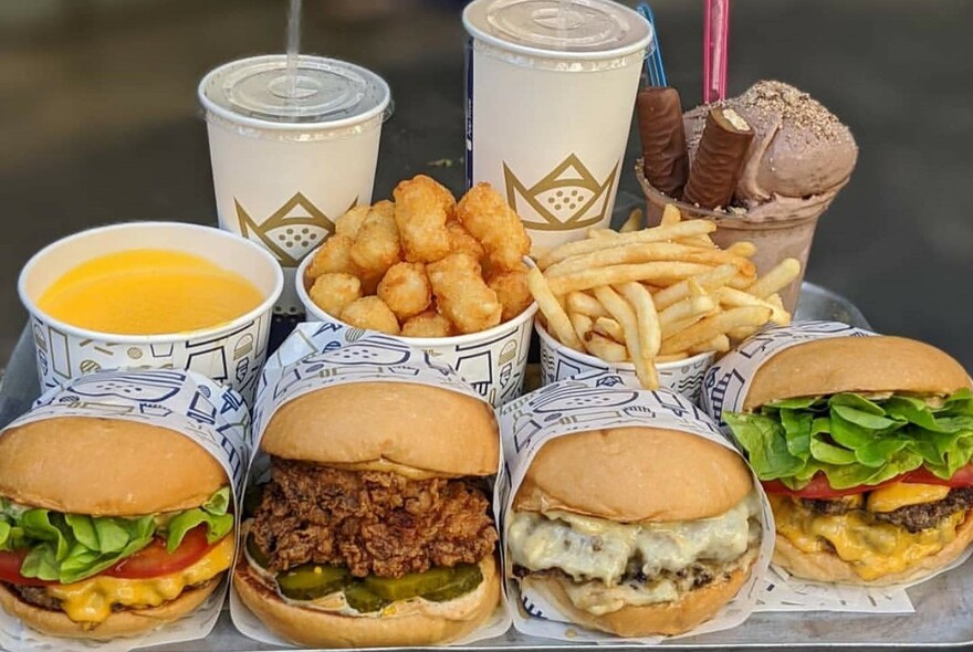 Four hamburgers in their wrappers, with chips, nuggets, soup, drinks and ice cream dessert.