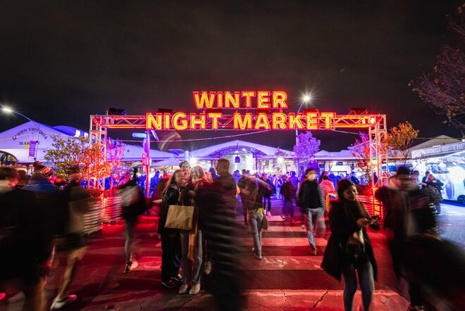 Arch in lights, with words in red, WINTER NIGHT MARKET, crowds in front.