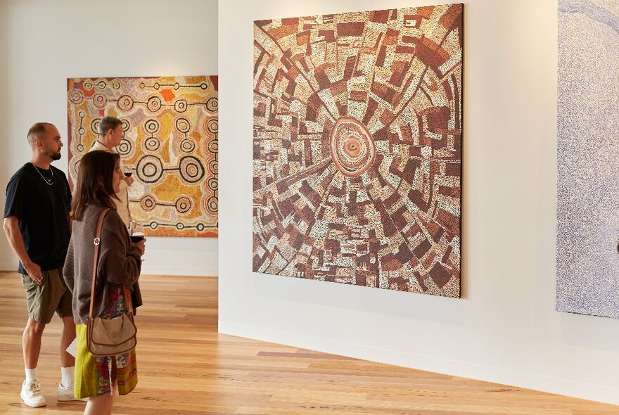 People inside an art gallery viewing large Indigenous paintings.