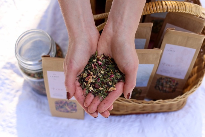A pair of hands outstretched holding herbal tea, with packets in a basket below.