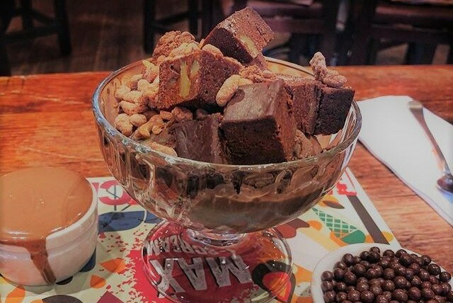 A glass bowl filled with ice cream and chocolate cake, with chocolate sauce on the side.
