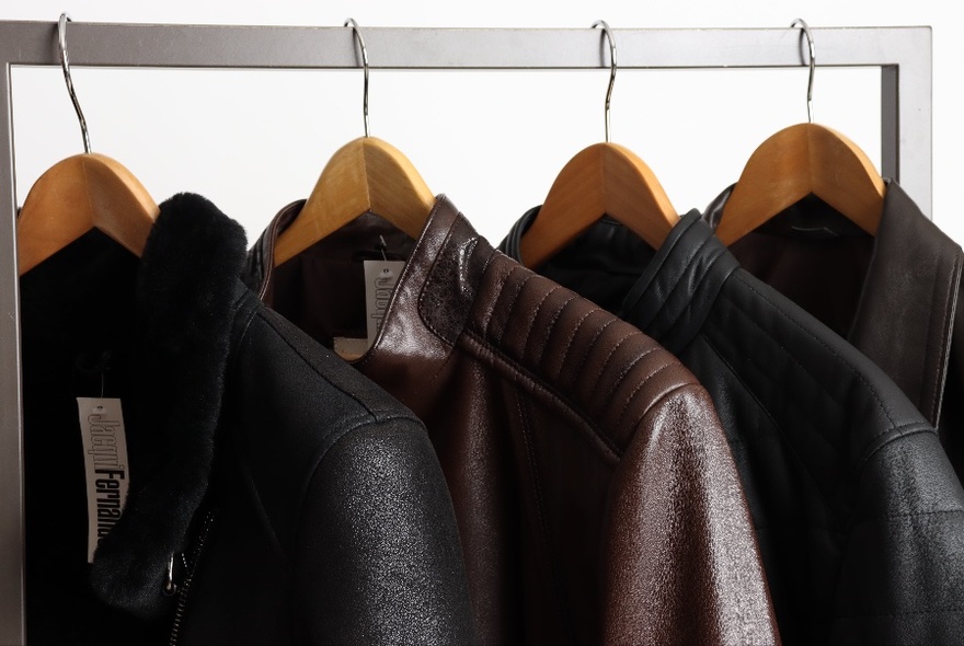 Dark leather jackets and coats on wooden hangers on a display rack.
