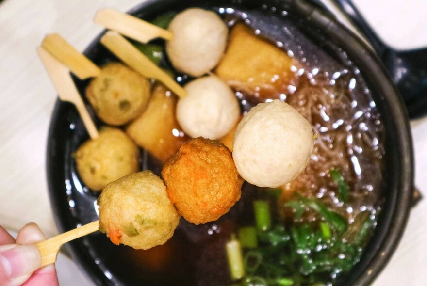 Hand selecting skewered fish balls from a hotpot.