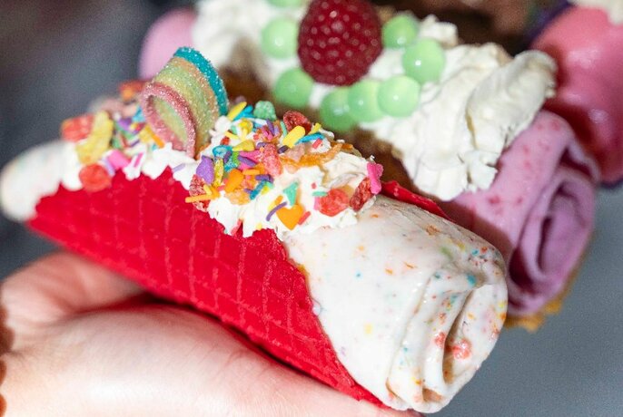 Open hand holding two colourful ice cream filled tacos, each decorated with candied frostings.